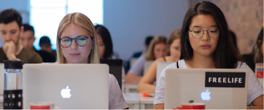 Two classmates working on their laptops during class